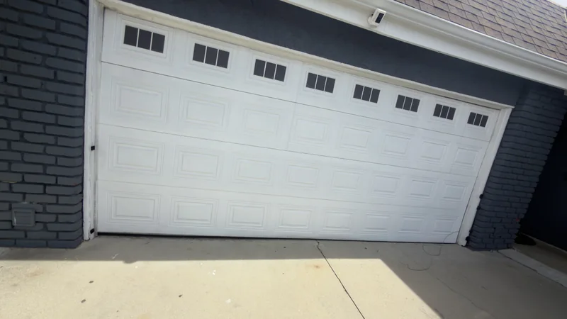 Wide white sectional garage door with divided windows and dark brick surrounds.