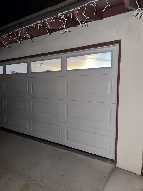 White sectional garage door with illuminated top windows at night.