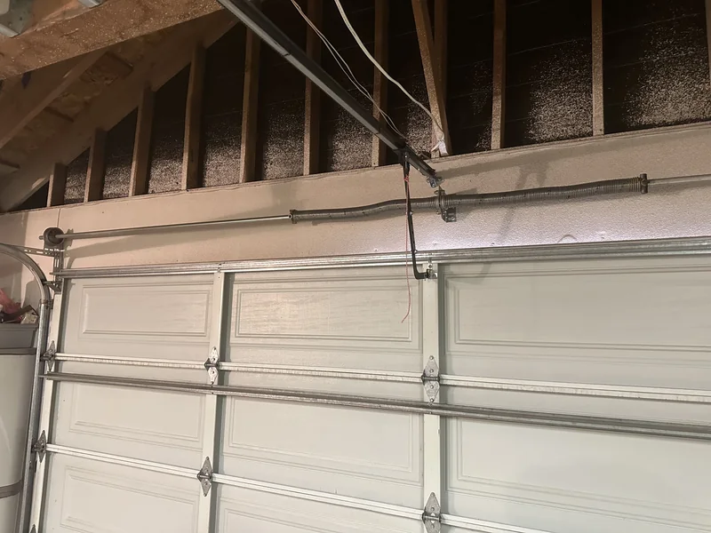 Interior view of a white sectional door with overhead torsion springs and exposed wall framing.